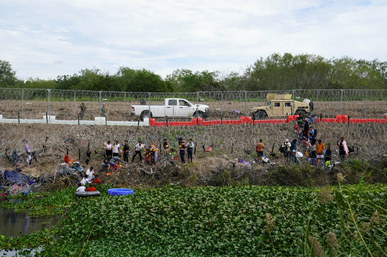 2023年12月29日，從墨西哥馬塔莫羅斯看到，人們在德克薩斯州布朗斯維爾的鐵絲網(wǎng)和新安裝的路障后面等待向美國邊境當局自首。