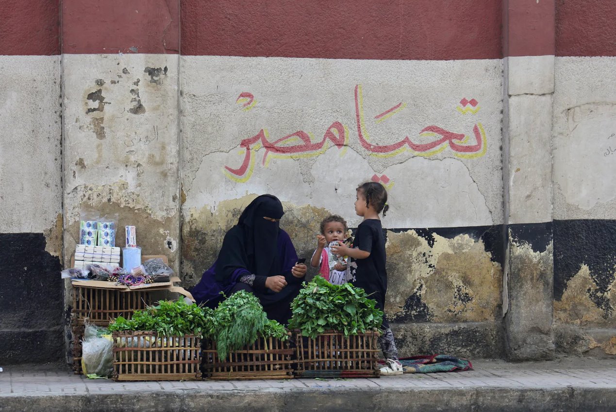 2023年10月10日，埃及開羅，一名帶著孩子的街頭小販坐在一幅壁畫前，壁畫上有埃及國旗和&ldquo;埃及萬歲&rdquo;的文字。