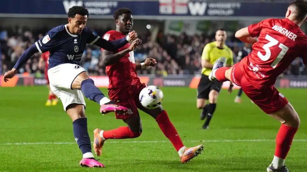 米爾沃爾隊的費米&middot;阿齊茲凌空抽射，伯明翰隊的凱&middot;瓦格納抬腳試圖封堵射門。